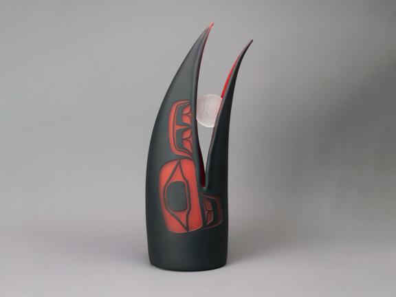 A stylized raven head holding a round piece of sand-blasted glass in its beak.