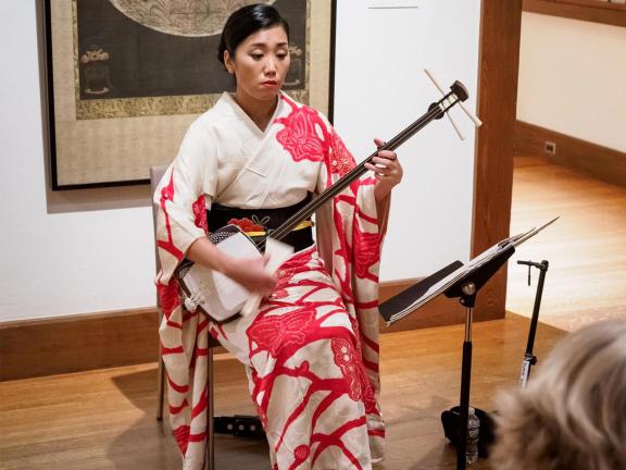 Seated musician wearing kimono and playing shamisen in Arts of Japan gallery