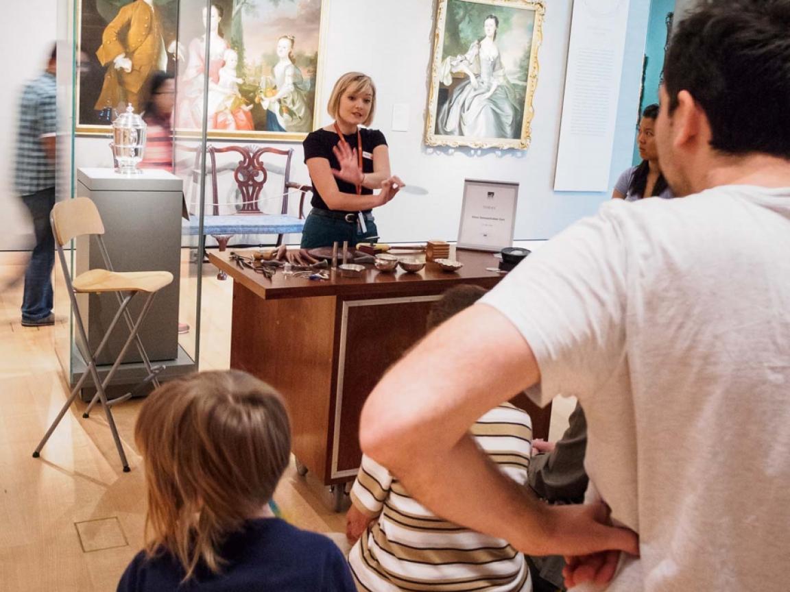 Instructor discussing silver pieces laid out on Artist Toolbox Cart in colonial America gallery