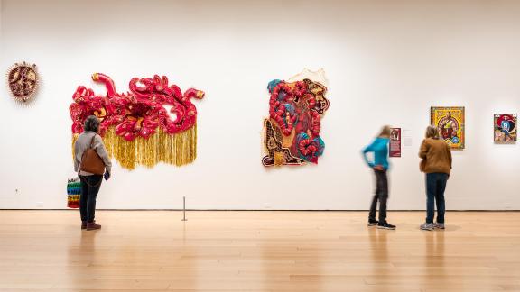 Visitors look at art on white walls.