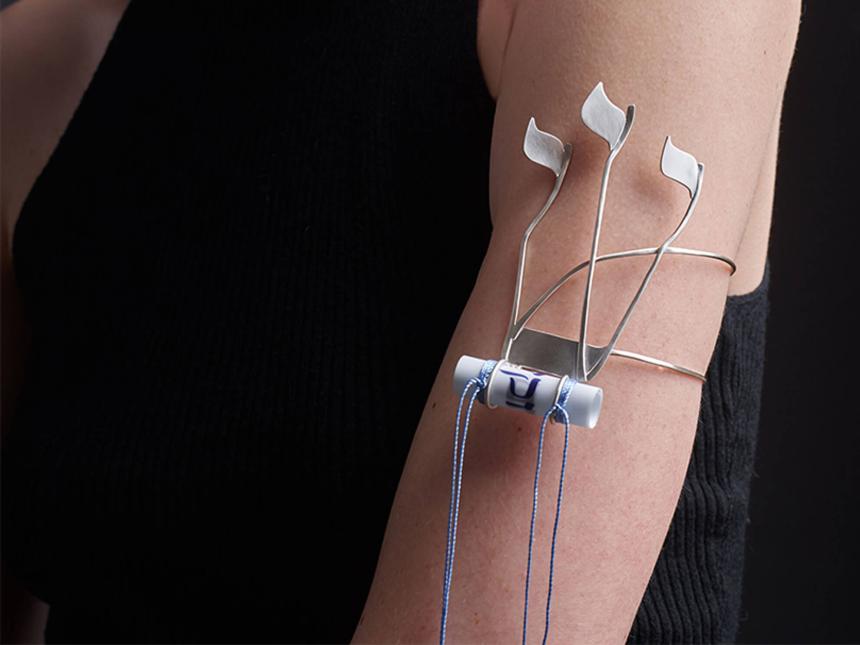 A woman wears a silver arm bracelet attached with a scroll of parchment imprinted with verses of the Torah and blue strings.