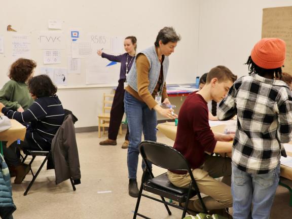 Teens making artwork in the studio while listening to a Museum Educator do a presentation. 