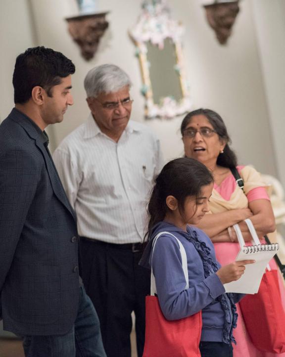 Multigenerational family standing in a gallery, with two kids holding sketchpads