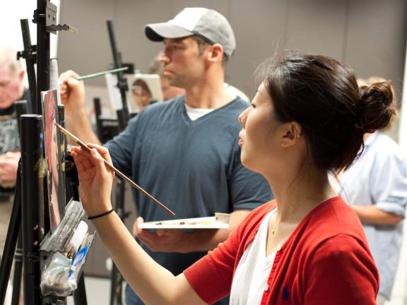 Two adult students paint on easels in classroom
