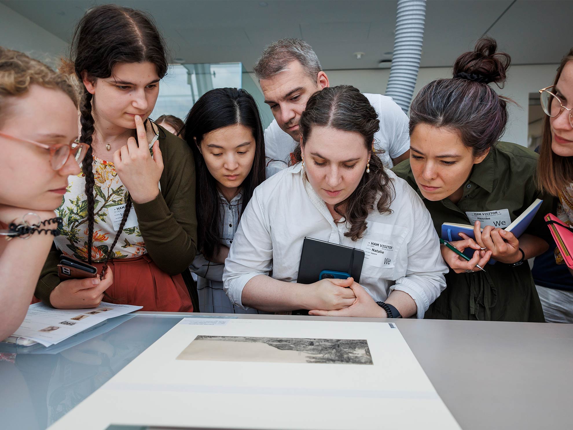 Group of students leaning in to take a close look at a piece of gold jewelry laid on a table