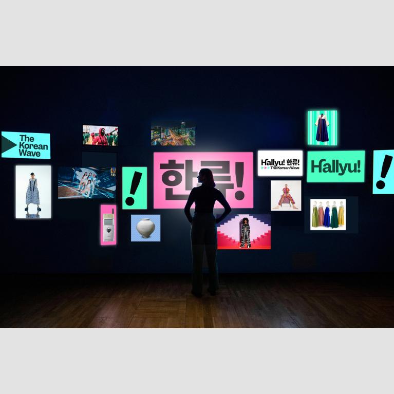 A woman stands in front of a video wall with 15 screens displaying different graphics and images that relate to "Hallyu! The Korean Wave."